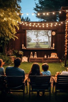 people sitting in lawn chairs watching a movie on the big screen at night with string lights