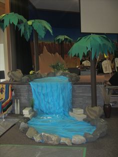 a fake waterfall in the middle of a room with two palm trees on either side