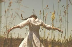 a woman in a white dress is standing in tall grass with her arms spread out