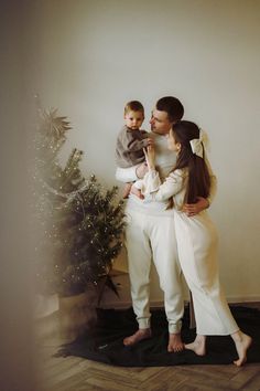 a woman holding a baby standing next to a christmas tree