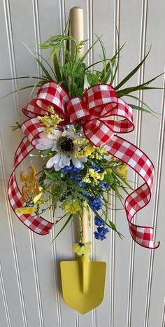 a red and white checkered bow hanging on the side of a door with flowers in it