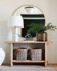 a white couch sitting next to a wooden table with baskets on it and a round mirror above it