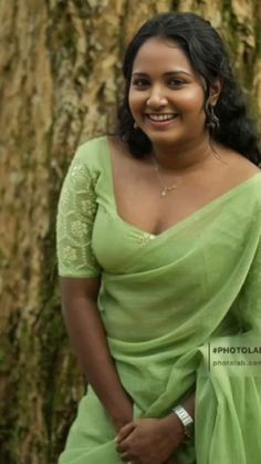 a woman wearing a green sari standing in front of a tree smiling at the camera