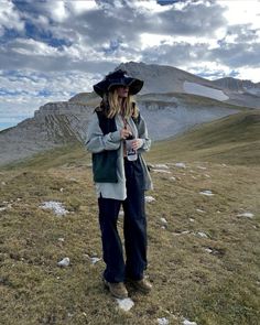 a woman standing on top of a grass covered hillside