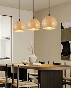 three lights hanging from the ceiling above a dining room table with chairs and a vase