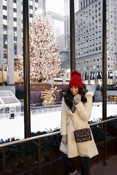 a woman standing in front of a christmas tree wearing a red hat and white coat