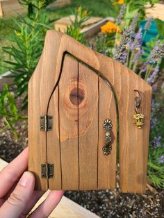 a hand holding up a small wooden house shaped like a door with two key chains attached to it