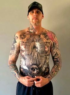 a man with many tattoos on his chest and arms standing in front of a wall