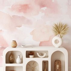 a white shelf with vases and bowls on it in front of a pink painted wall