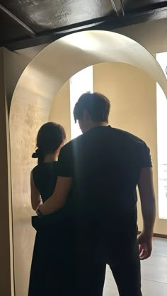 a man and woman standing in front of an arch looking at something on the wall