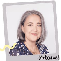 an older woman with gray hair and blue shirt smiling at the camera, in front of a welcome sign