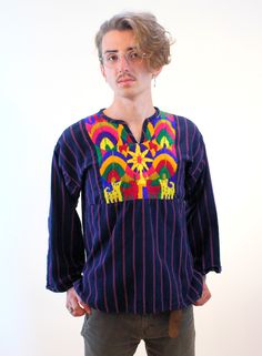 This is an incredible 1960s vintage Guatemalan top with cute embroidered cats! It's a deep purplish-blue indigo color sturdy cotton with vertical purple stripes, and the front chest panel is thickly handwoven with yellow kitty cats, pink deer, some small pink animals that might be sheep, and a colorful, abstract, sunny landscape. This bohemian shirt is a pullover with a small V neck, wide sleeves and side vents.  It's in good clean condition, freshly laundered, with light wear - a few minor pulled yarn threads and a hand stitched repair on the side seam under the right sleeve. No other issues or flaws noted. The label says "Lankin, 100% Algodon, Hecho en Guatemala." We recommend hand washing separately in cold water and line drying. It fits like a Women's Medium or Men's Small based on the Hippie Long Sleeve Top With Boho Collar, Relaxed Fit Multicolor Embroidered Tops, Embroidered Cotton Shirt For Festival, Cotton Embroidered Shirt For Festival, Cotton Long Sleeve Tops With Boho Collar, Cotton Boho Collar Long Sleeve Tops, Cotton Long Sleeve Top With Boho Collar, Bohemian Multicolor Crew Neck Shirt, Hippie Long Sleeve Cotton Shirt