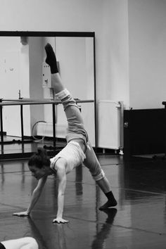 two women doing yoga poses in a dance studio, one on her back and the other upside down