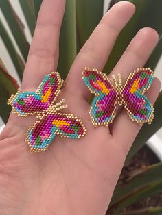 two colorful butterfly shaped earrings sitting on top of a person's hand