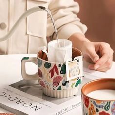 a person is pouring water into a cup on top of a table next to a book