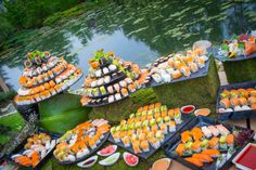 an assortment of sushi on display in front of a pond with water and trees