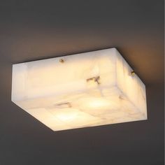 a square light fixture mounted on the wall in a room with grey walls and flooring