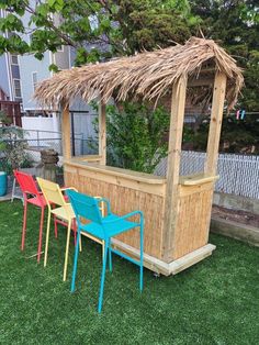 some chairs and a table in the grass near a building with a straw roof on top