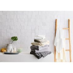 a stack of folded towels sitting on top of a bath tub next to a wooden ladder