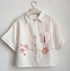 a white shirt with red flowers on it hanging from a hanger against a wall