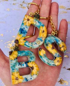 a hand holding three yellow and blue letters with sunflowers on them in front of a white background