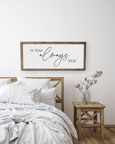 a bed with white sheets and pillows next to a wooden sign that says it was always you