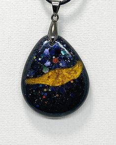 a black and yellow pendant on a white surface with blue speckles, gold trimming