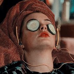 a woman with cucumbers on her eyes laying in a towel and listening to headphones