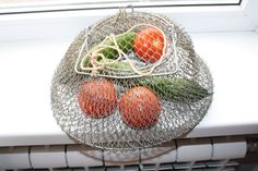 four tomatoes and two cucumbers in a wire basket on a window sill