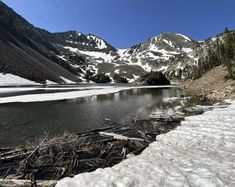 the snow is covering the ground and water in the mountains near a lake with ice on it