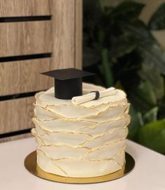 a white cake with a black graduation cap on top, sitting on a gold plate