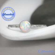 "This delicate Sterling Silver Opal Promise Ring features a 6 mm cabochon that has been carefully set in a highly polished fine silver bezel. The band is made of a sturdy round Sterling Silver wire that has been given a hammer texture, then carefully polished for a bright finish. Our setting process involves carefully tightening the fine silver bezel down around the stone, then beveling at the edge of the bezel to further compress the silver, creating a water-tight seal with no stone movement. T Minimalist Round Cabochon Opal Ring, White Gold Opal Cabochon Ring, White Gold Cabochon Opal Ring, White Opal Ring With Bezel Setting, White Birthstone Ring Gift With Round Stone, Silver Opal Stackable Rings As Gift, White Opal Stackable Round Rings, Silver Stackable Opal Ring As Gift, Stackable White Gold Opal Ring As Gift