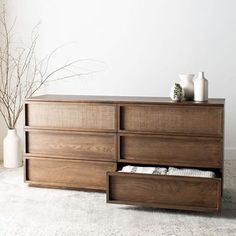 a large wooden dresser with drawers and vases on it's top, in front of a white wall