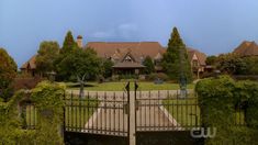 an iron gate in front of a large house with trees and bushes surrounding the entrance