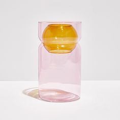 a yellow vase sitting on top of a white table next to a glass container filled with liquid