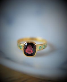 This lovely garnet ring is accented with contrasting chrome diopside embedded in to the band. The garnet is a magenta tone that will color change with the light and the chrome diopside are a bright spring green. A lovely eye catching combination that is fresh yet classic. 14k solid gold. January birthstone. Garnet: 2.57 carats total, 8 mm x 6 mm Size 5.75-6 Due to the embedded stones in the band, this ring cannot be resized to anything larger than a 6.0. Ready to ship. Elegant Tourmaline Birthstone Ring With Bezel Setting, Classic Emerald Ring With Gemstone Accents For May Birthstone, Tsavorite Rings With Gemstone Accents For Anniversary, Formal Multi-stone May Birthstone Ring, Tourmaline Birthstone Rings For May, Anniversary Tsavorite Birthstone Ring With Gemstone, Classic Tourmaline Jewelry For May Birthstone, Formal Tourmaline Birthstone Jewelry, Formal Multi-stone Ruby Ring With Tourmaline