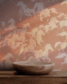 a bowl sitting on top of a wooden table in front of a wall with horses painted on it