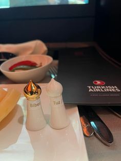 a plate with two salt and pepper shakers next to a bowl of fruit on the table