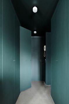 an empty hallway with blue walls and green doors on both sides, leading to a phone booth