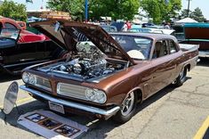 an old car with its hood open in a parking lot full of other cars and people