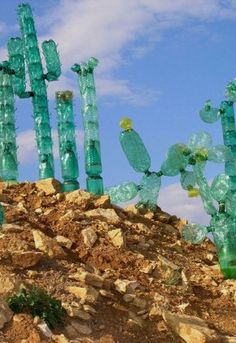 green glass cactus sculptures sitting on top of a rocky hill under a blue cloudy sky