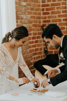 the bride and groom are cutting their wedding cake at the reception table in front of the brick wall