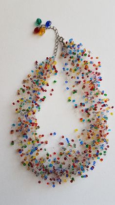 a multicolored beaded necklace hanging from a chain on a white surface with beads