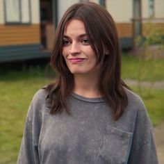 a woman with long brown hair standing in front of a house and looking at the camera