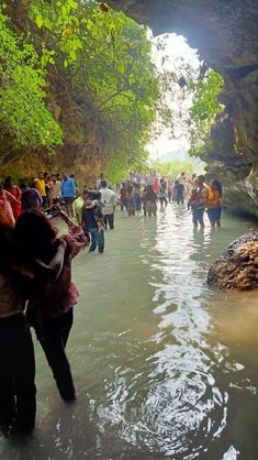 many people are walking in the water near some rocks and green trees on either side