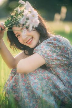 a woman in a floral dress holding flowers up to her face and smiling at the camera