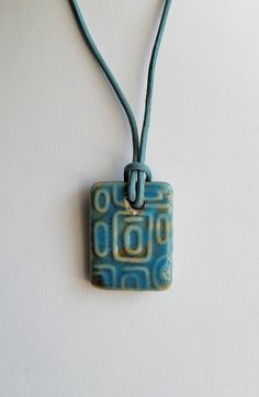 a blue square shaped ceramic pendant hangs from a cord