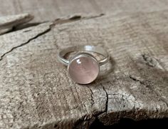 A beautiful round pink rose quartz sits in sterling silver with a handmade ring band from sterling silver half dome wire. Choose from either a simple setting or a more floral scallop setting. The rose quartz cabochon is 11mm in size. Rose quartz is a stone that promotes healing, love, and attraction. It can draw love to the the wearer, help heal from heartbreak, and help sustain feelings of love and romance. Made to order, stones vary with slight differences in color, lines, etc. Rose Gold Moonstone Ring In Sterling Silver, Rose Gold Sterling Silver Moonstone Ring, Pink Moonstone Sterling Silver Ring For Anniversary, Round Rose Quartz Promise Ring, Pink Sterling Silver Moonstone Promise Ring, Round Rose Quartz Rings For Anniversary, Rose Quartz Round Rings For Anniversary, Adjustable Round Rose Quartz Jewelry, Pink Round Moonstone Ring For Gift