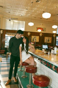 a man standing next to a woman sitting at a counter in a restaurant with stools