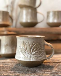 a white coffee cup sitting on top of a wooden table next to other mugs